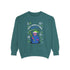 A holiday sweatshirt featuring a cute Grim Reaper holding a scythe, wearing a Santa hat. Above the character is the text "Grave Tidings We Bring," surrounded by festive snowflakes and holiday-themed designs. The combination of spooky and festive elements adds a humorous twist to traditional holiday attire.